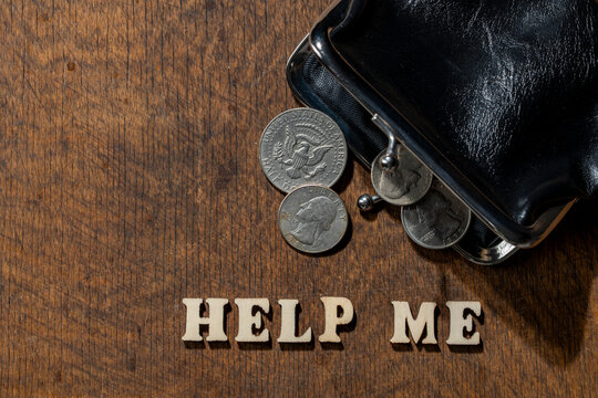 Empty black leather wallet with US dollar coins spilling onto rustic wooden table next to the words HELP ME, closeup. Perfect for social security, inflation, bankruptcy, and financial crisis concepts