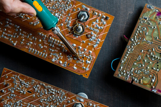 Closeup of technician's hand soldering components on vintage electronic circuit board with green soldering iron. Ideal for repair services, engineering, and DIY electronics concepts