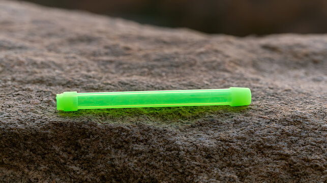 Bright green plastic glow stick lie flat on rough natural stone background, ready for emergency use during night camping trip or party event