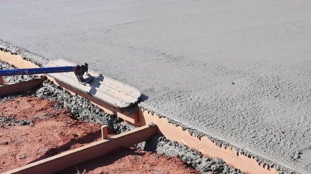 Masonry worker works on concrete slab using trowel at abuilding site is uneven with stones around.
