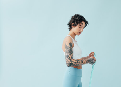 Young slim woman performing resistance band stretching exercises over a clean blue studio background