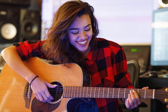 Cheerful woman playing on acoustic guitar in a music studio