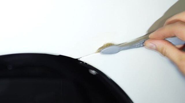 Detailer using a brush to clean dirt from the car fender gap.
