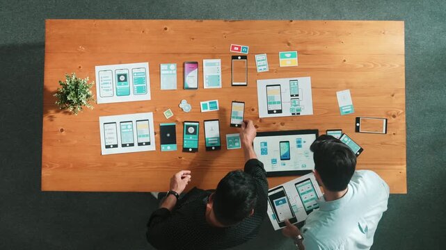 Software developer team holding software icon and discussing about Ux Ui design for mobile phone interface. Top view of programmer work together to brainstorm wireframe prototype design. Convocation.