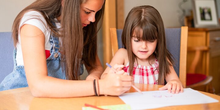 Woman helping a young girl with drawing at a table in a cozy room.