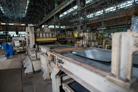 Industrial factory interior with heavy machinery processing metal sheets under high ceiling with steel beams and natural light