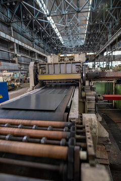 Industrial metal processing machinery in large factory hall with steel beams and conveyor system
