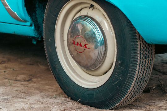 Gomel, Belarus - 08.08.2026: A close-up view of a classic car wheel featuring a cream rim, black rubber tire, and a chrome hubcap with red ZMA lettering, mounted on a turquoise vintage vehicle.