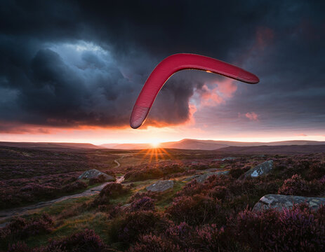 A red boomerang floating in a dramatic cloudy sky over a moorland landscape at sunset.