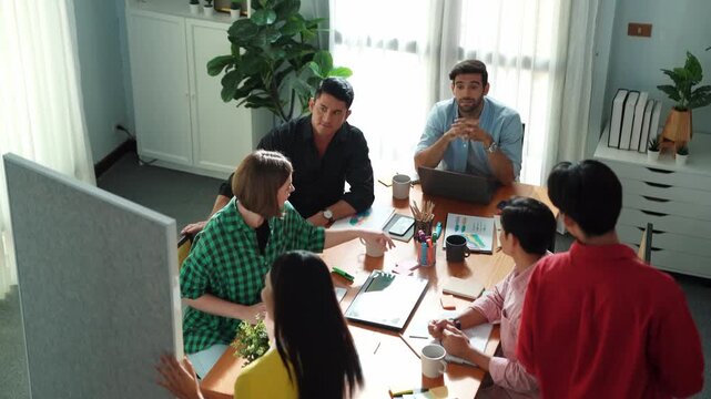 Top view of manager present idea while colleague helping explain idea and answering question. Group of skilled diverse people listen presentation while raising hand for asking question. Convocation.