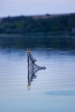 Black fishing keepnet on a rod stand submerged in calm reflective lake water