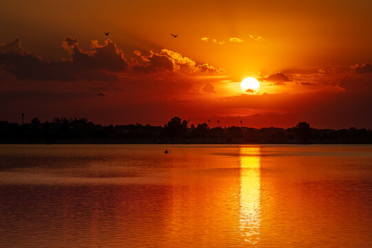 Dramatic orange sunset over Lacul Morii lake in Bucharest with kayakers silhouette.