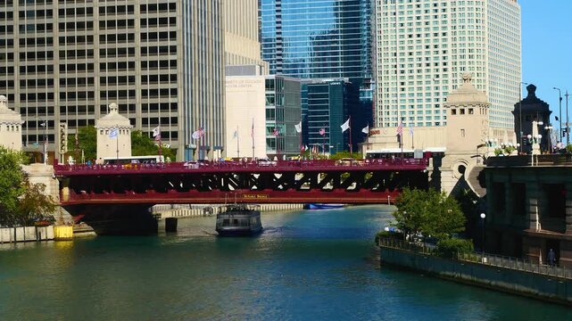 Scenic view of the Chicago River flowing through downtown, featuring iconic skyscrapers, historic bridges, and tour boats navigating the urban waterway on a sunny day.