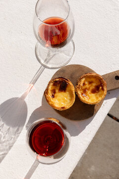 Portugese egg tart served on a wooden cutting board with glass of port wine on a patio with afternoon shadows