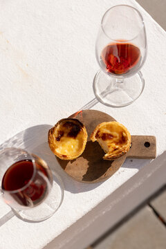 Portugese egg tart served on a wooden cutting board with glass of port wine on a patio with afternoon shadows