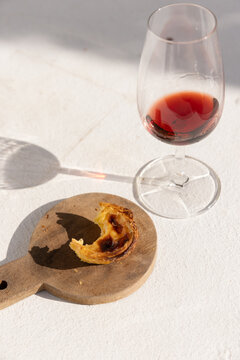 Portugese egg tart served on a wooden cutting board with glass of port wine on a patio with afternoon shadows