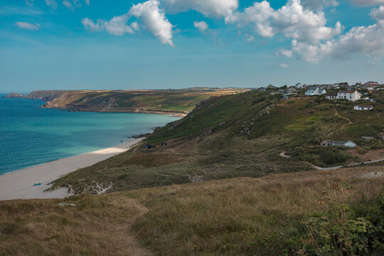White sand beach and turquoise water of Whitesand Bay near Sennen Cove in Cornwall, with green cliffs and clifftop houses.