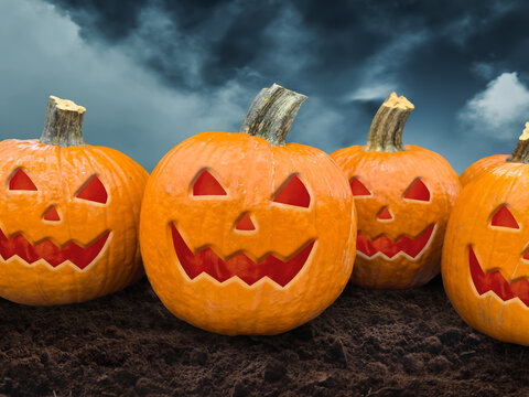 Multiple scary carved Jack-o-lanterns resting on dark soil under a moody stormy sky
