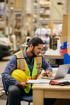 Young warehouse manager using laptop while working in storage room.