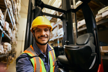 Happy man working as fork truck operator in warehouse and looking at camera © Drazen