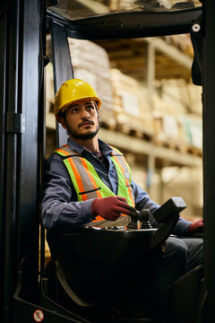 Young forklift operator working in storage compartment at warehouse.