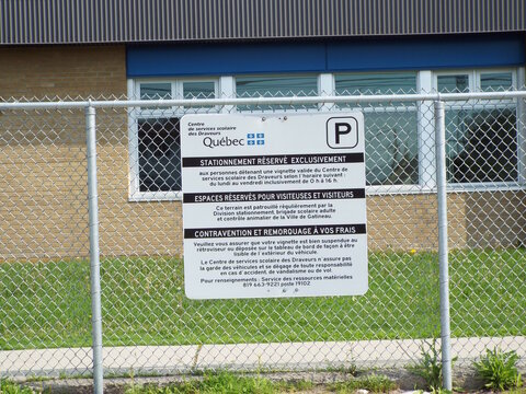 Gatineau, Quebec, Canada &ndash; July 02, 2026: A bilingual parking regulation sign posted on a chain-link fence outlines reserved parking rules for the "Centre de services scolaire des Draveurs" on boul. S