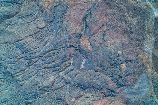 Grey slag heap surface with radial erosion ridges and deep gullies, top view aerial shot