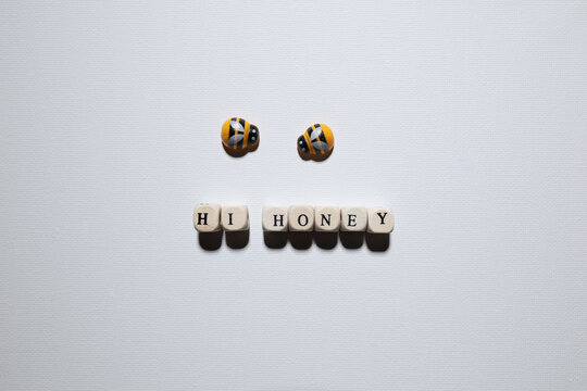 Flat lay of two bee figures above wooden letters spelling &ldquo;HI HONEY,&rdquo; creating a playful greeting and affection concept with copy space.
