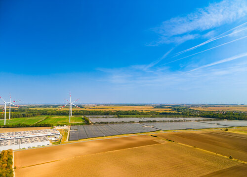 Wind turbines and solar farm in rural landscape. Aerial view of wind turbines and solar panels near agricultural fields, blue sky.