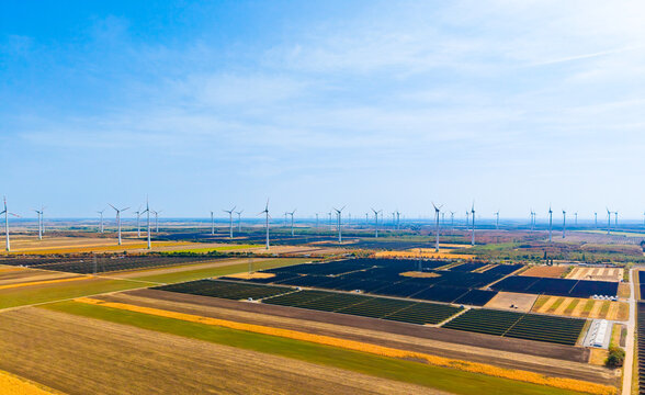 Large renewable energy complex with wind and solar. Panoramic aerial view of solar panels and wind turbines on vast agricultural land.