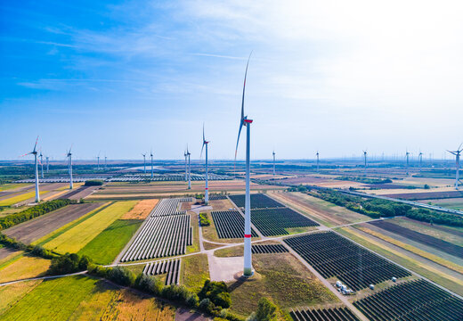 Hybrid renewable energy, solar panels and wind turbines on field. Aerial landscape view showing solar panel array and multiple wind generators under bright sun