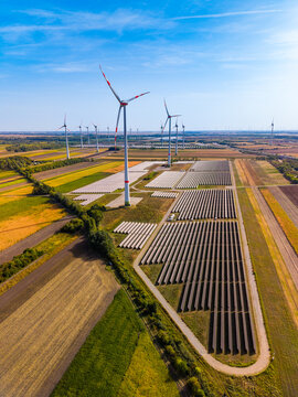 Aerial view of solar panels and wind turbines. Top down aerial view of large solar array, wind turbines, surrounding farm fields under clear blue sky, daylight.