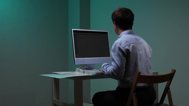 Young man sitting at a desk, typing on a computer keyboard in a dimly lit office setting, concentrating on his work during late hours or an intense project