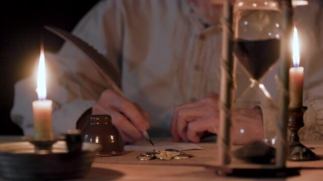 man writing with a quill pen with a pile of old coins on the table