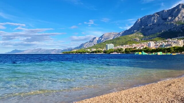 The turquoise water of the Adriatic Sea breaking on the Makarska town main pebble beach and the Biokovo mountain, Croatia, in sunny summer day