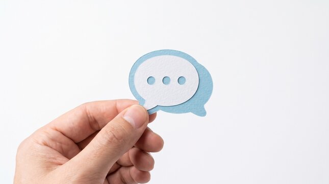 Hand holding a blue and white paper speech bubble with three dots representing conversation or thinking
