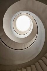 Fototapeta premium Spiral staircase viewed from below with round skylight at top. Minimalist concrete architecture with geometric circular shapes and natural light.