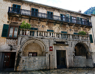 The ornate stone facade of the historic baroque Bizanti Palace features stone loggias, balustrades, and green window shutters in Kotor, Montenegro © Gregory