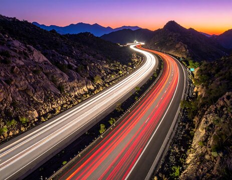 Long exposure photograph of a winding mountain highway with glowing car light trails at sunset. Perfect for logistics, travel, and transportation design projects.