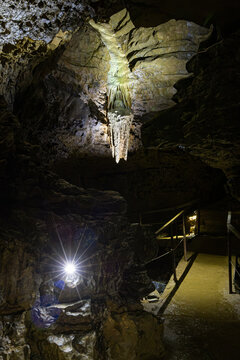 Illuminated hanging stalactite speleothem suspended above a tourist walkway and safety railing in the Lurgrotte cave system in Peggau, Styria
