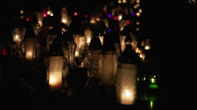 Glowing memorial candles burning at a cemetery during All Saints Day at night
