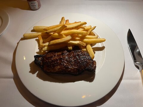 Grilled steak with french fries on a white plate served at a restaurant dinner table