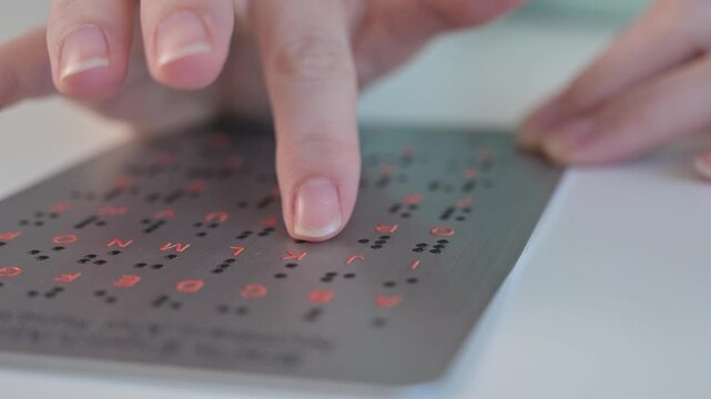 A blind woman learns the English alphabet from a braille sign.