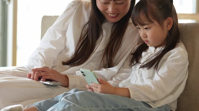 リビングでスマートフォンを使う女の子とお母さん