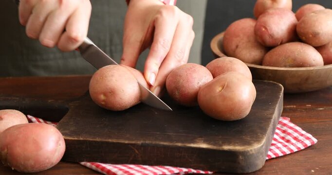 Woman cutting ripe red potato at table, closeup