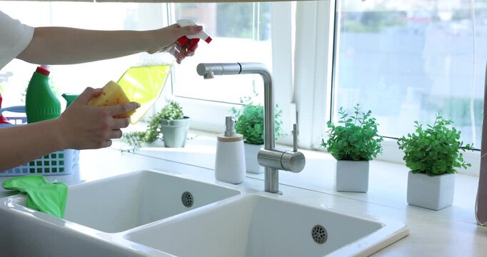 Woman cleaning faucet with detergent and sponge in kitchen, closeup