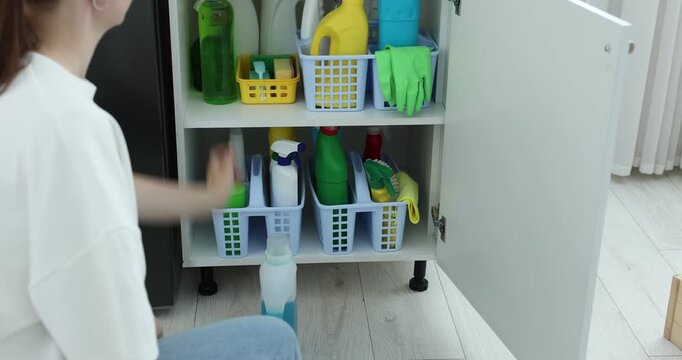 Woman putting detergents into cabinet with different cleaning products and supplies indoors, closeup