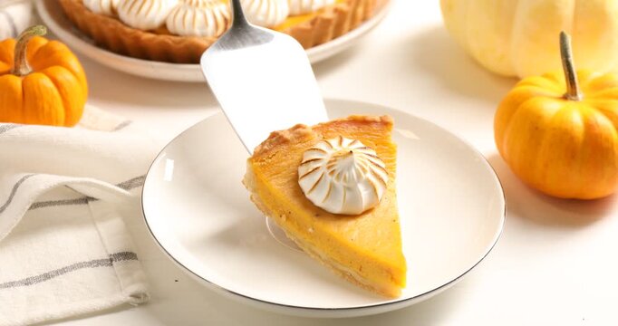 Putting piece of delicious pumpkin pie with meringue onto plate at white table, closeup. Pastry for Thanksgiving day or other fall holiday