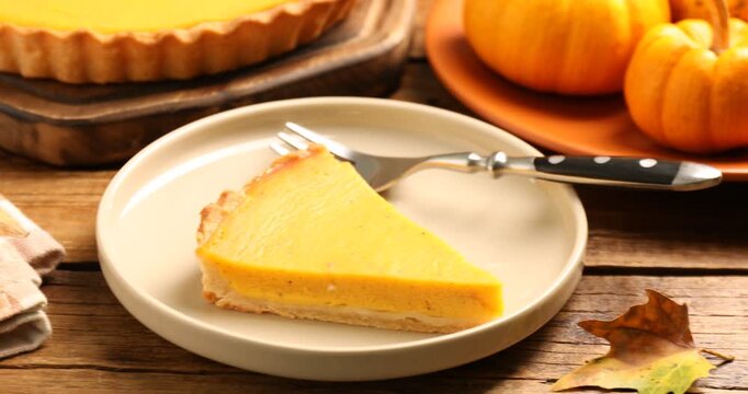 Pastry for Thanksgiving day or other fall holiday. Delicious pumpkin pie and leaves on wooden table, closeup. Camera moving right