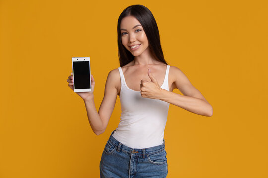 Happy woman presenting smartphone with blank screen and thumbs up